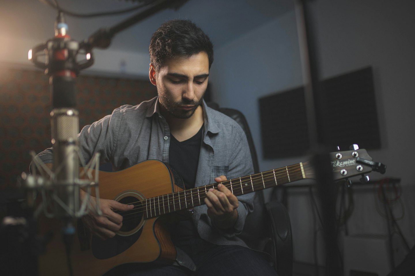 Man playing an acoustic guitar in a recording studio.